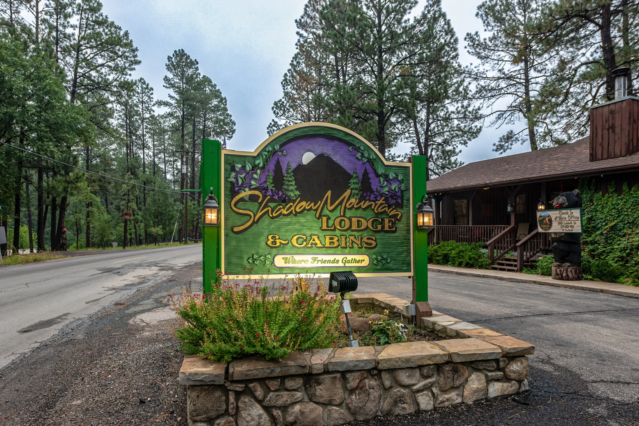 Entrance sign for Shadow Mountain Lodge & Cabins in Ruidoso welcoming guests to the mountain lodge surrounded by towering pine trees along the roadside